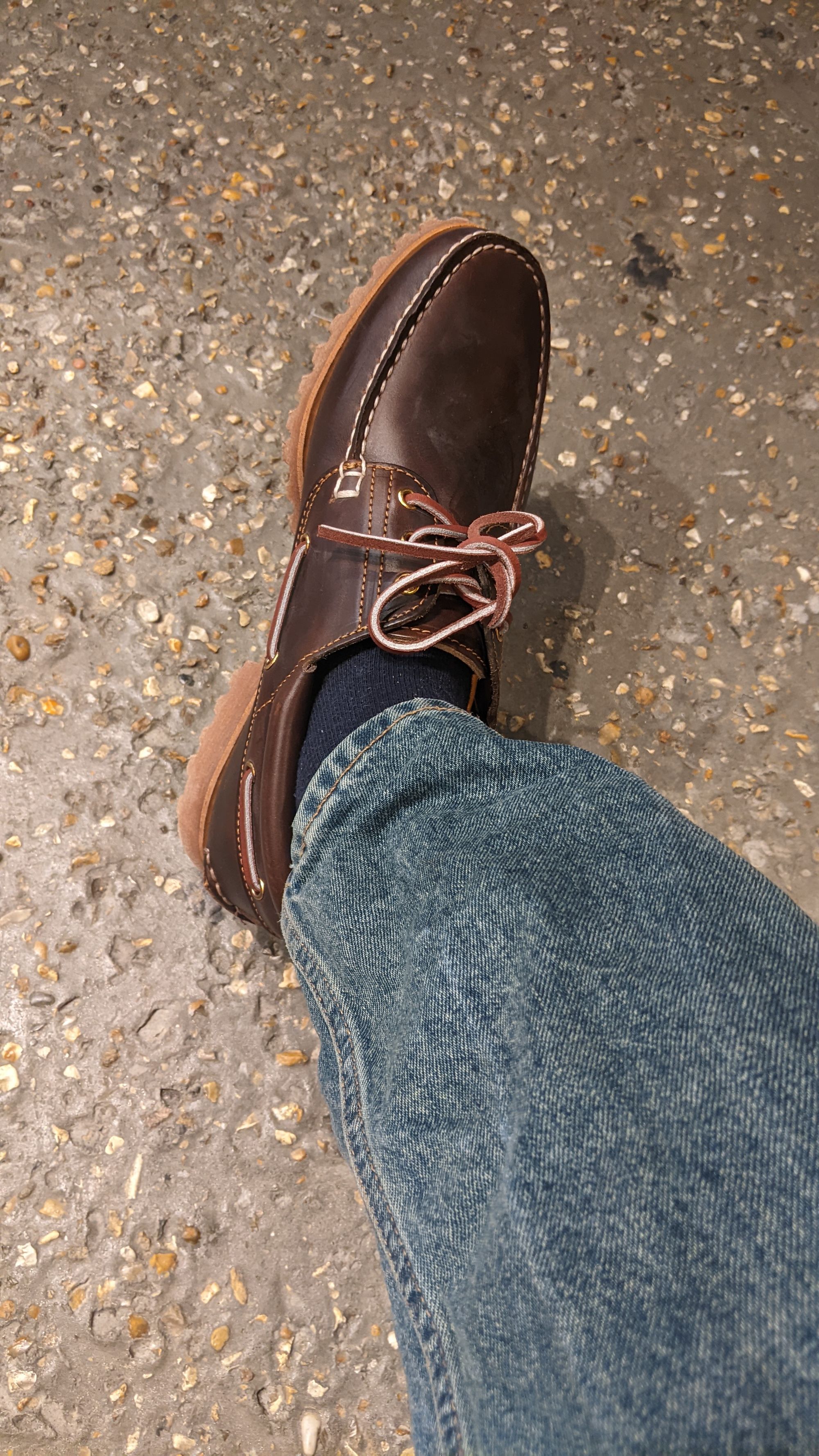 A brown shoe attached to a leg with blue jeans