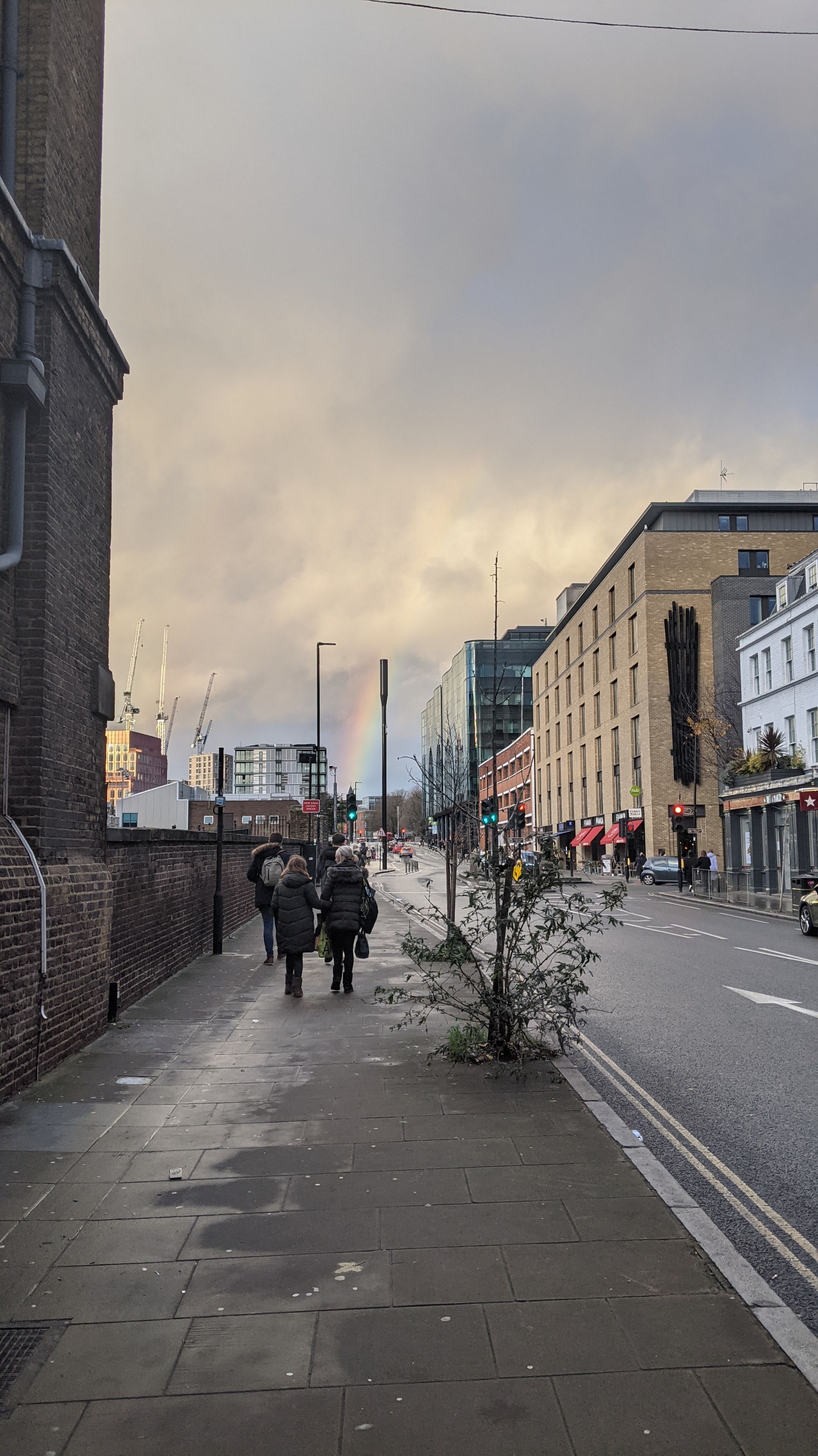 Picture of a street with a rainbow at the end coming down from the clouds